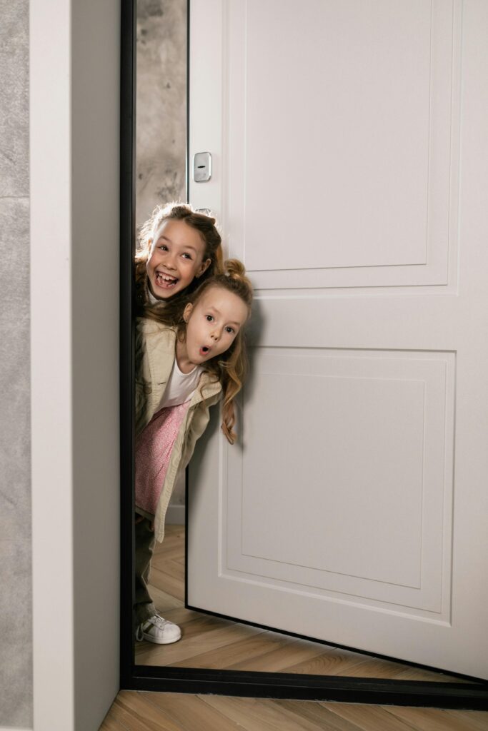 Two young girls happily play peekaboo through a door. Perfect for family and childhood themes.